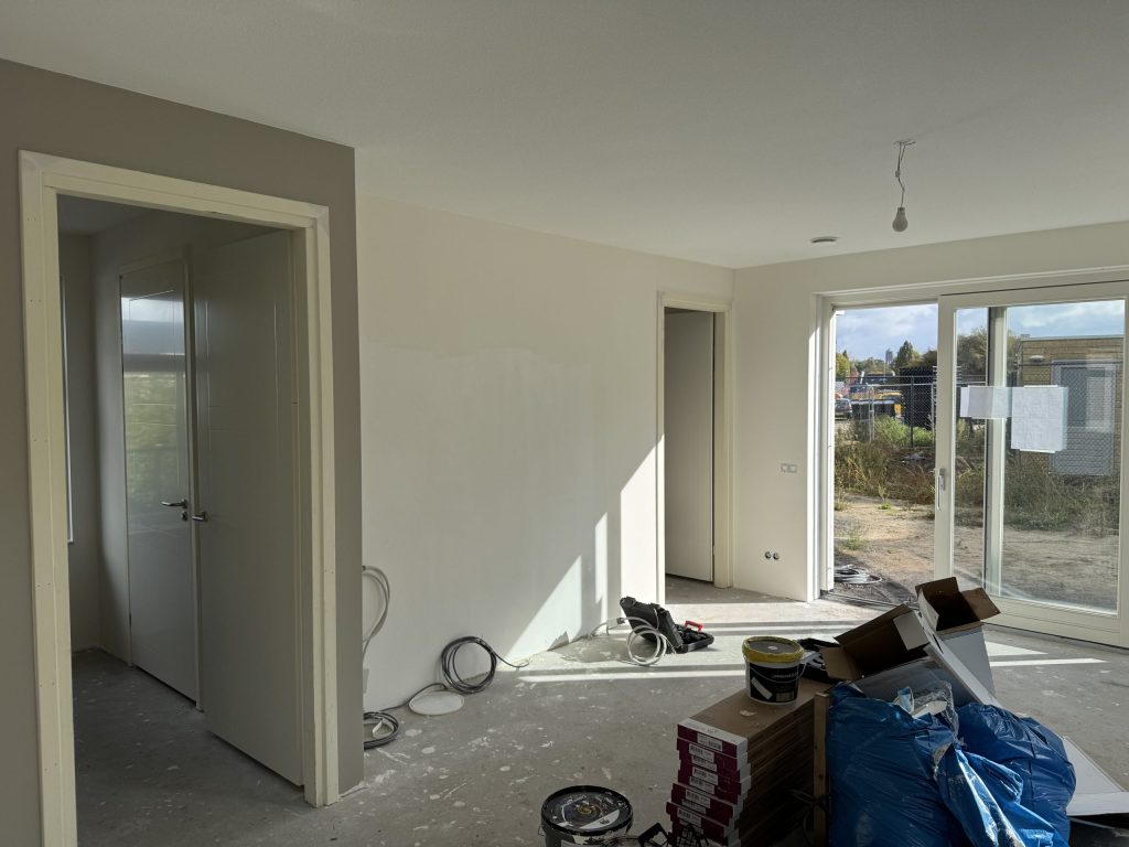 Nieuwbouwwoonkamer tijdens de afwerking met schuifpui, verfemmers en dozen op de betonvloer