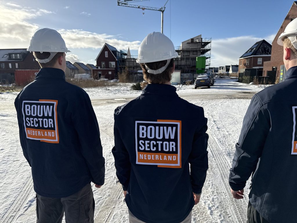 Drie medewerkers van Bouwsector Nederland met witte helm tussen nieuwe woningen in aanbouw